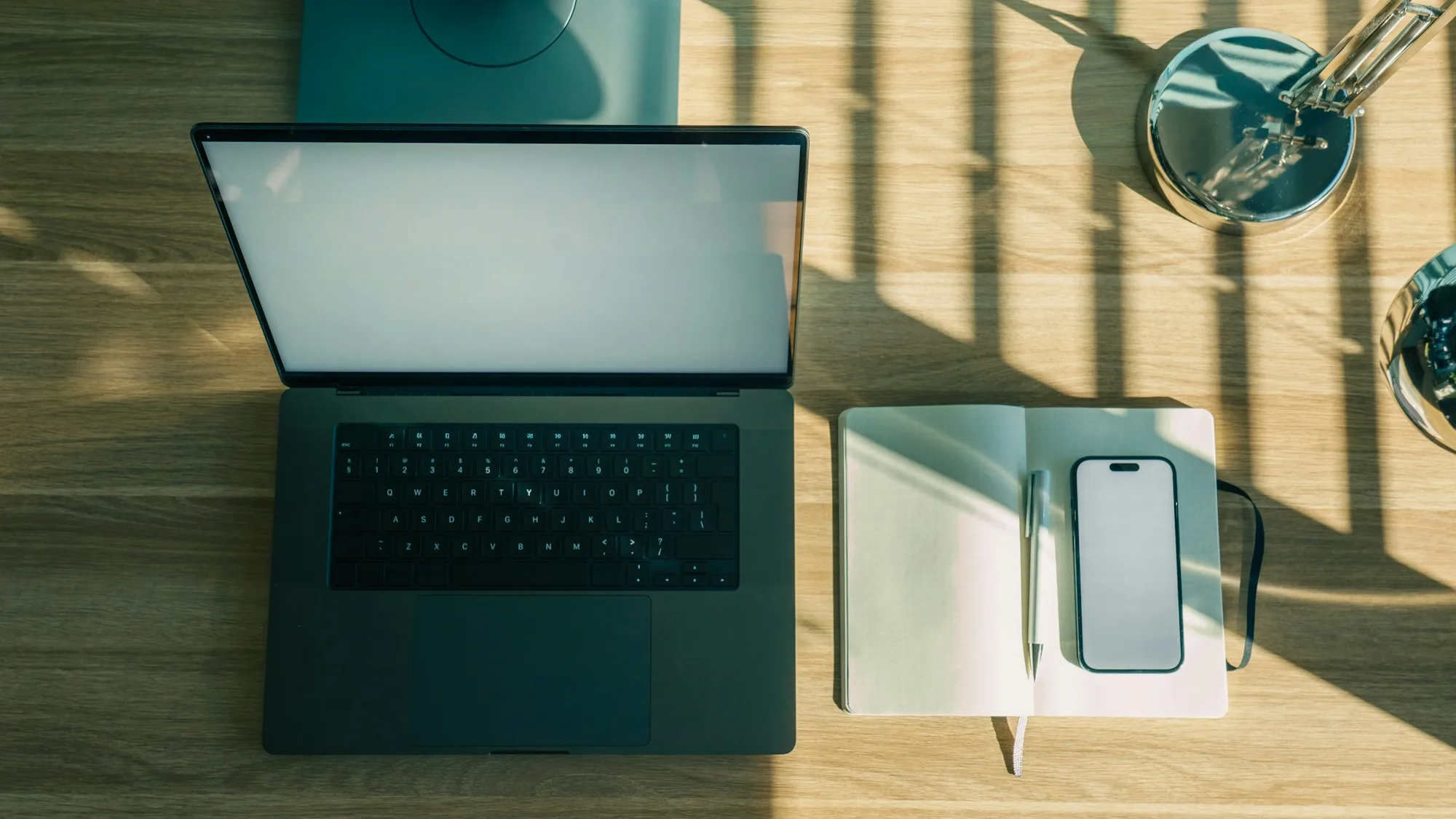 Laptop, Smartphone und Notizbuch auf einem sonnigen Schreibtisch